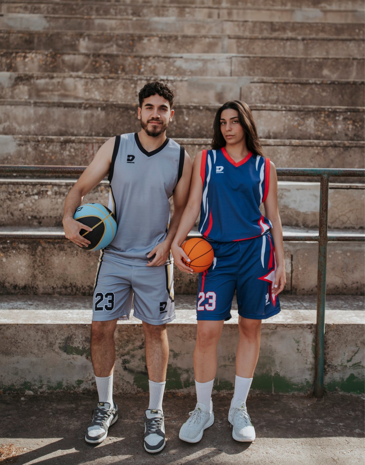 Due giocatori con kit da basket Dinicri davanti alle gradinate di un campo all'aperto